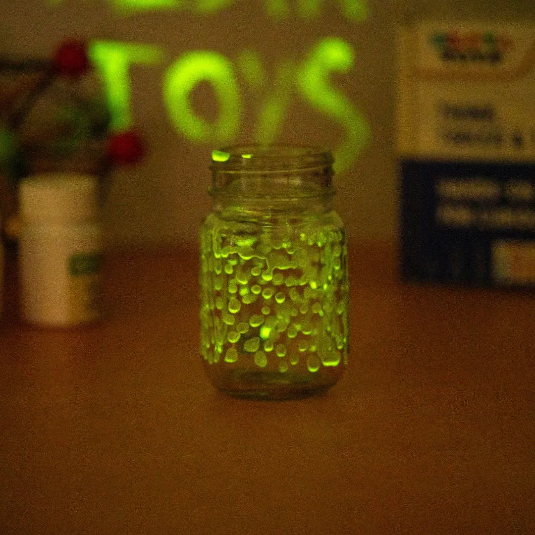 Glass jar filled with glowing green beads shining in the dark during a glow in the dark science experiment for kids
